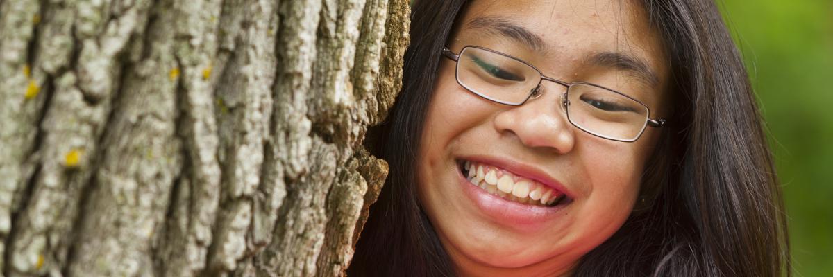 un gros plan d'une jeune fille qui grimpe à un arbre en souriant. Elle porte des lunettes.