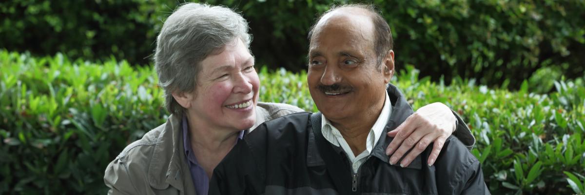 Un homme aveugle et une femme souriante assis sur un banc.