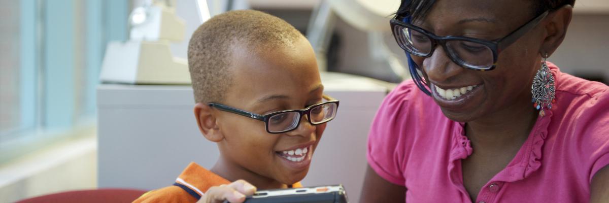 A young boy and his mother, both wearing glasses, interact as the little boy plays with a magnifier. 