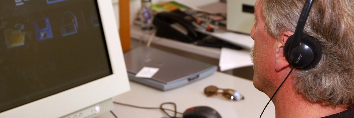 Un homme utilisant Zoomtext sur son ordinateur et ayant des écouteurs sur les oreilles