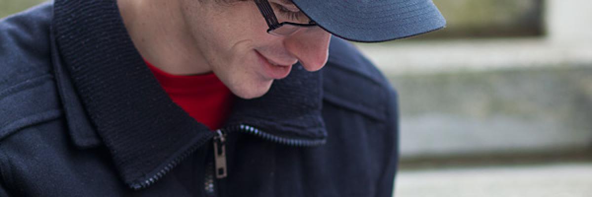 Homme lisant avec la loupe rouge et se portant une casquette noire.