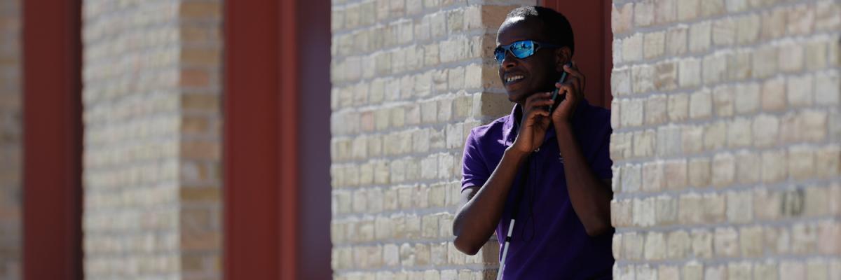 A young man holds a white cane in one hand and an iPhone in another. 