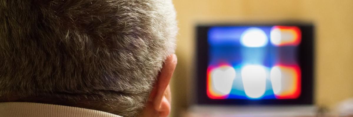 Homme aux cheveux gris regardant une télévision embrouillée.