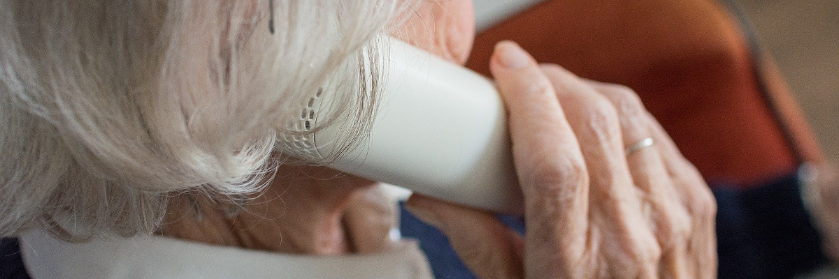 Une femme aînée porte un téléphone avec fil à son oreille.