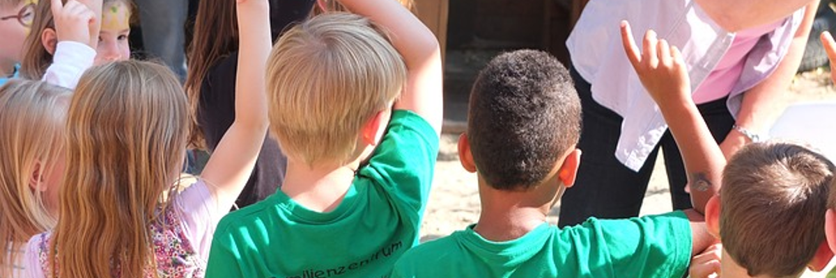 A group of young children raise their hands in the air to answer a question.