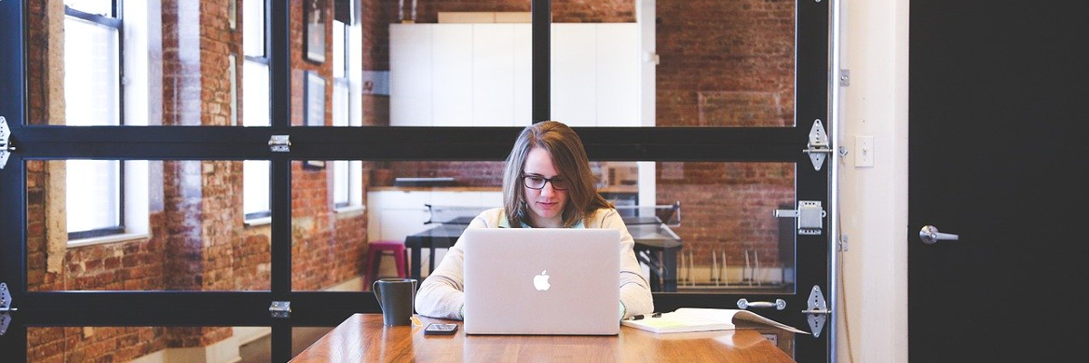 A young woman sits alone in a boardroom. She is busy typing on her laptop