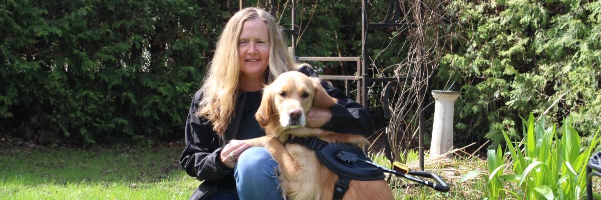 Diane Bergeron kneeling on grass next to her guide dog Carla, a golden retriever.