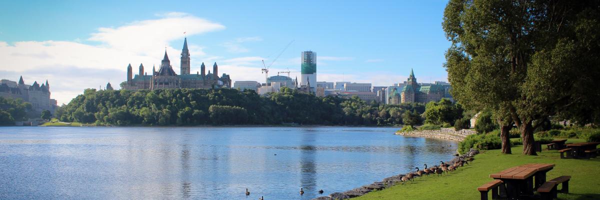 Une table de pique-nique accueillante dans un parc longeant le canal Rideau avec le Parlement canadien en arrière-plan.] 