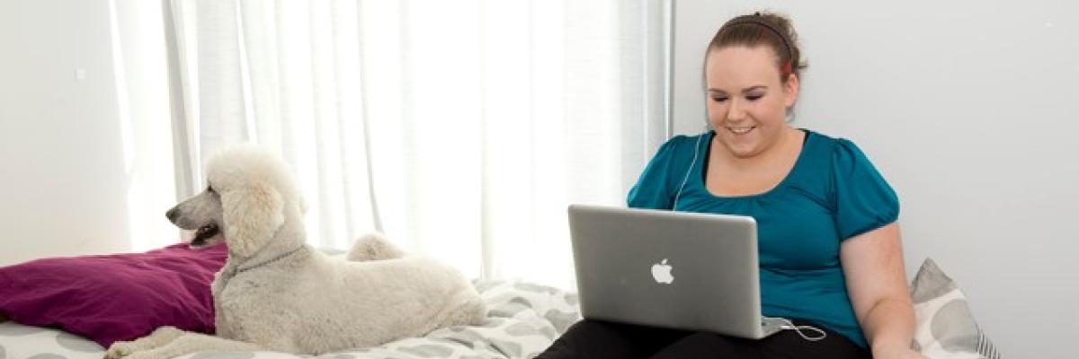 Woman sits on bed using laptop