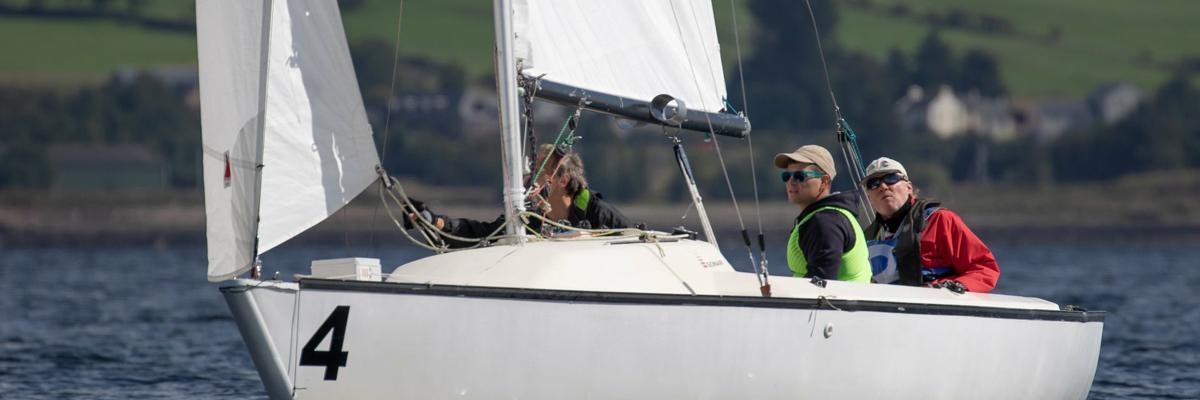 Joshua Cook and two other people sit in a sail boat on the water. They are at the World Blind Sailing Championships in Scotland.