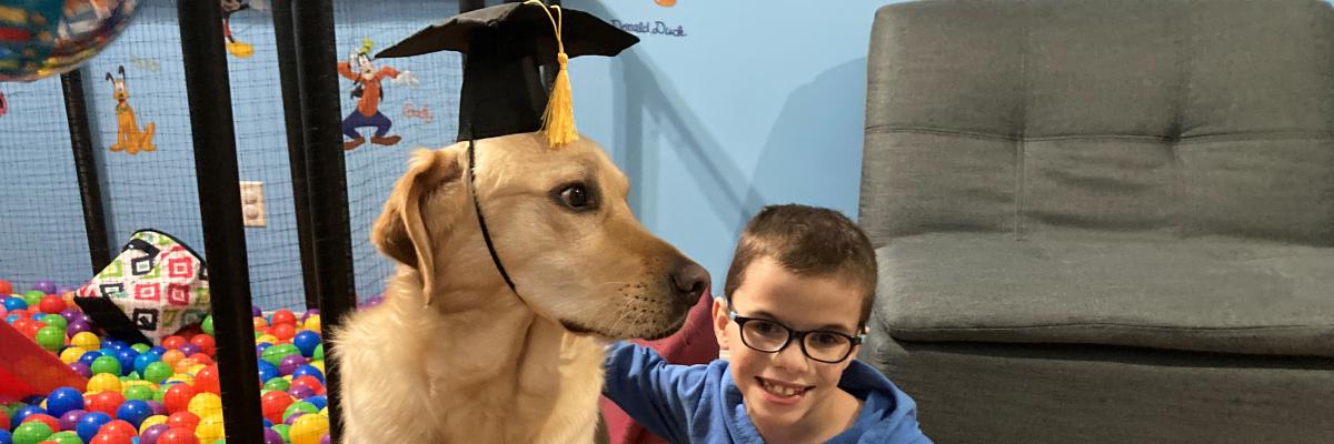 Un jeune portant des lunettes à genoux à côté de son chien compagnon portant un mortier.