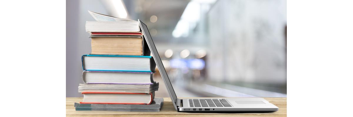 Une pile de livres à côté d'un ordinateur portable posés sur une table en bois.