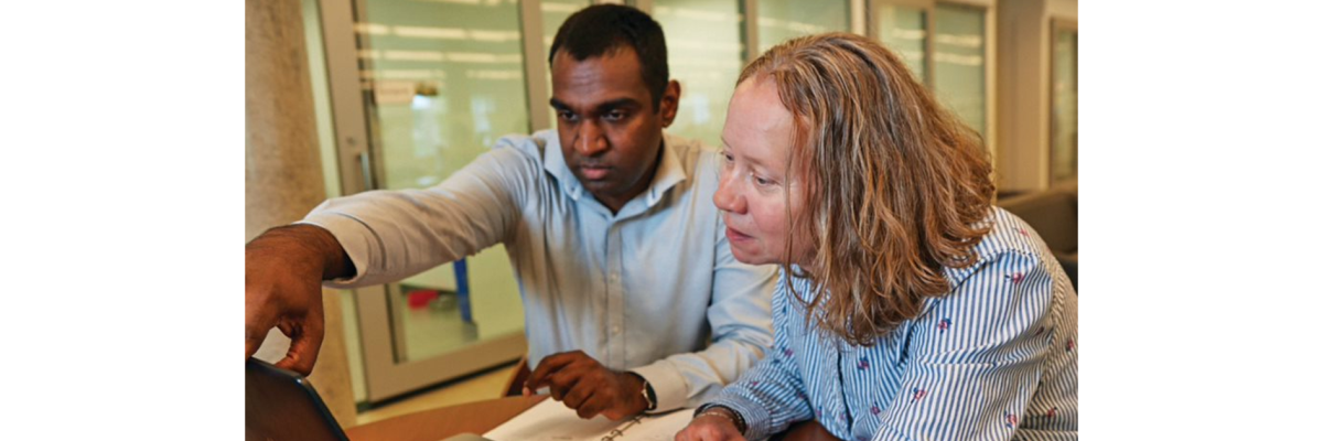 A man and a woman sitting at a desk looking a laptop screen 