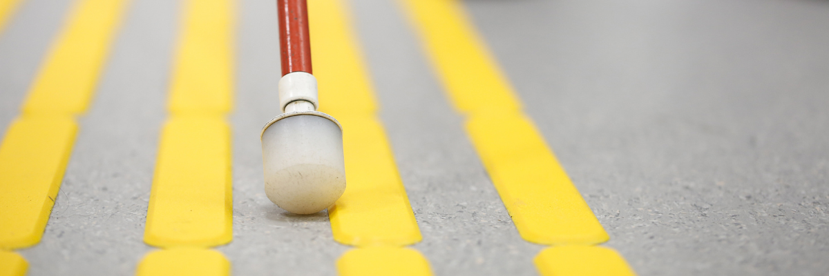 Une canne blanche utilisée sur une chaussée avec des lignes jaunes surélevées.