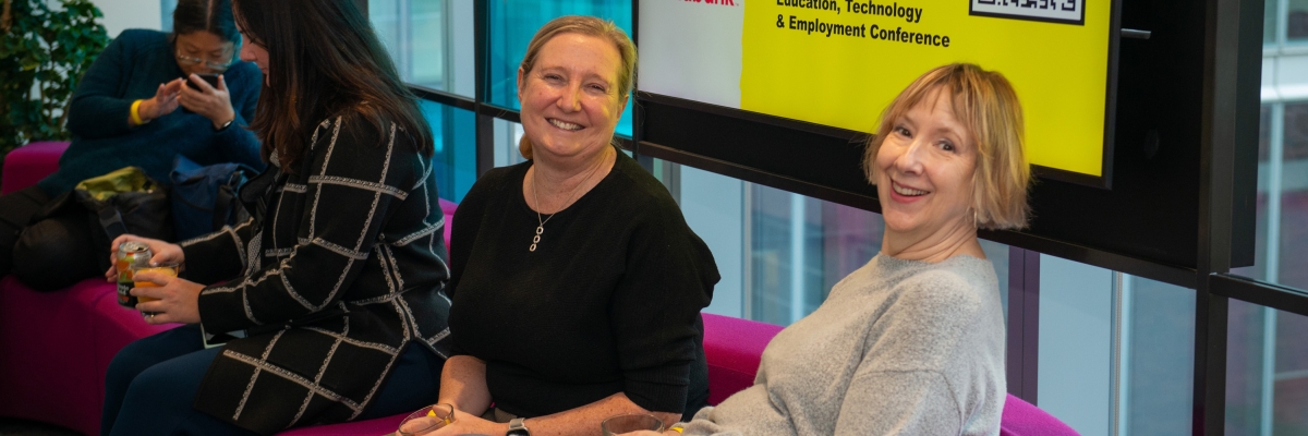 Deux femmes sont assises sur un canapé avec un panneau Connecting the Dots derrière elles. 