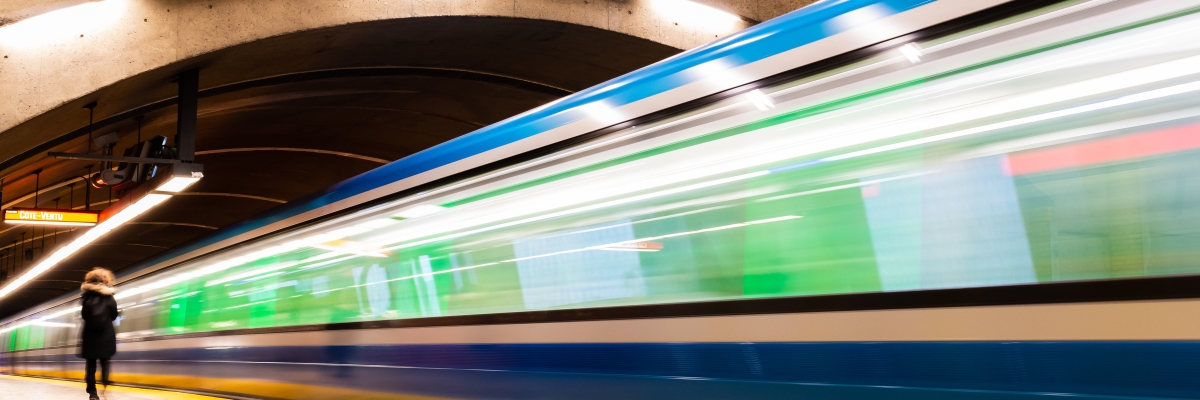 Un train entre dans une gare intérieure vide. L'image est floue et mal cadrée, suggérant que le train est en mouvement à l'approche de son arrêt. Le plafond de la gare est incurvé et éclairé, et une personne marche sur le quai