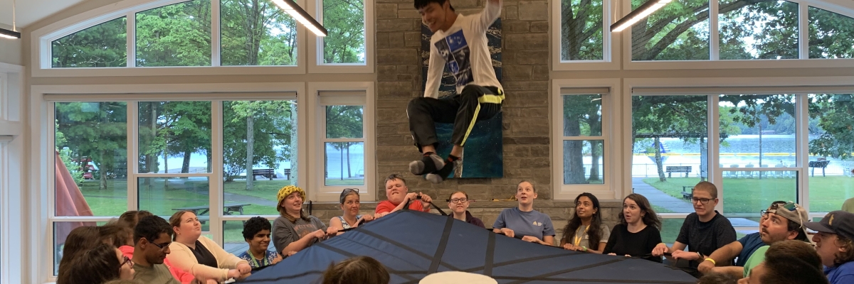 Des campeurs d'été tiennent un trampoline en cercle après avoir lancé un campeur dans les airs.