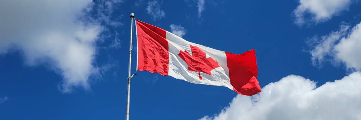 Un drapeau canadien flotte au sommet d'un mât, sur fond de ciel d'un bleu éclatant.