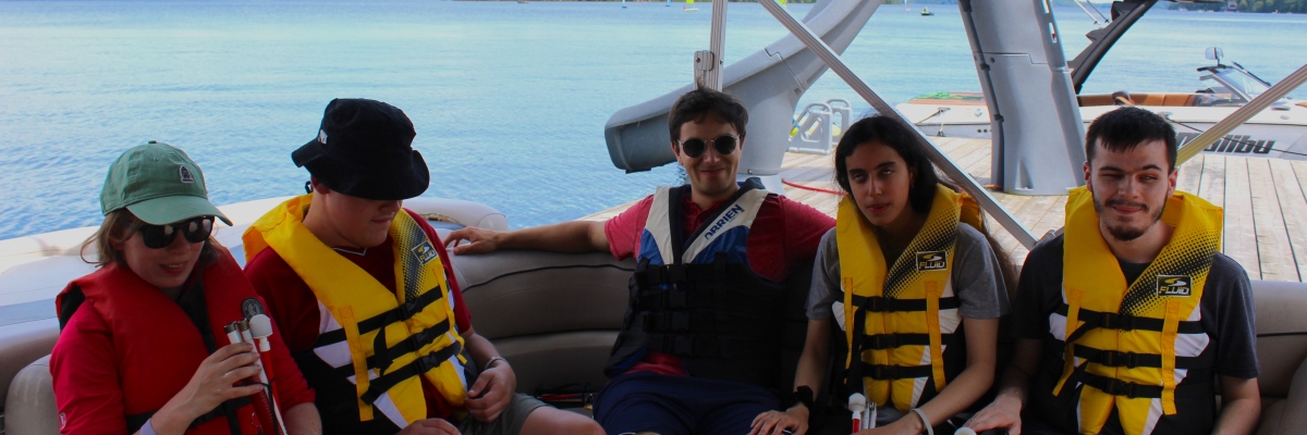 5 jeunes adultes portant une veste de sauvetage sur un bateau.
