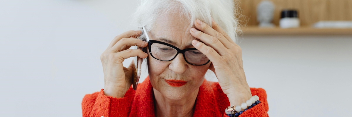 Une femme âgée est au téléphone et se tient la tête, l'air dépité.
