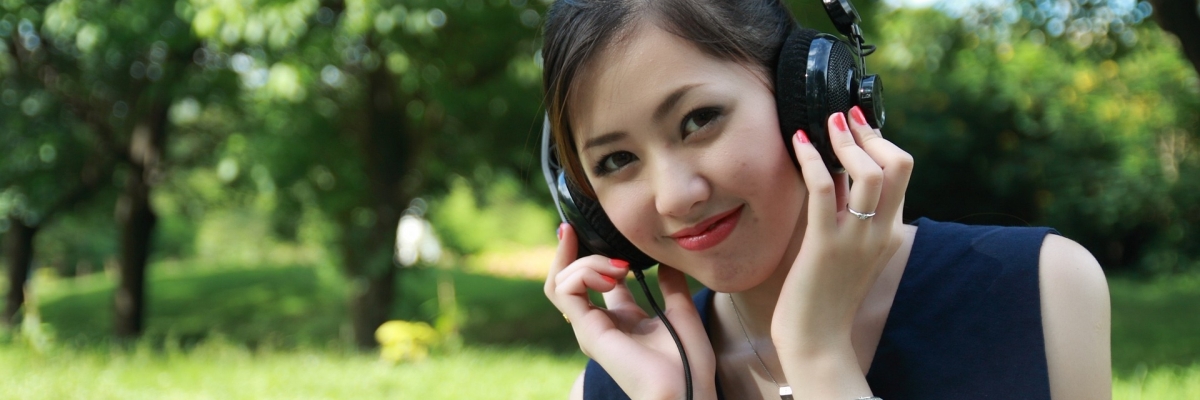 Une fille dans un parc porte un casque d'écoute et sourit.