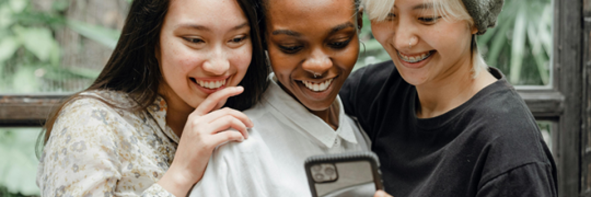 Trois jeunes femmes sur un téléphone cellulaire sourient.