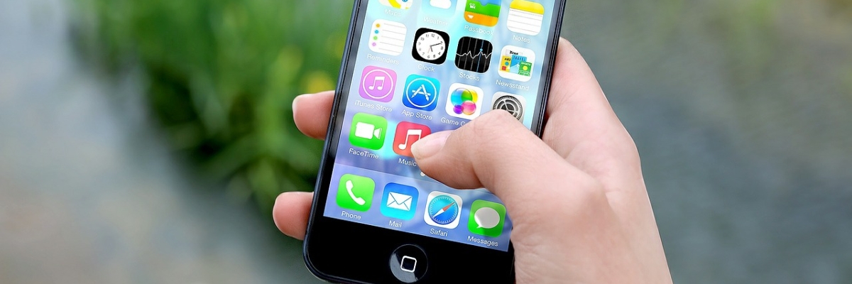 Main tenant un iPhone. Des icônes d'applications apparaissent à l'écran.