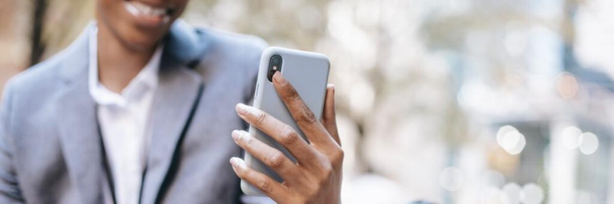 Femme noire assise sur un banc de parc, portant une veste d'affaires et tenant son téléphone intelligent.