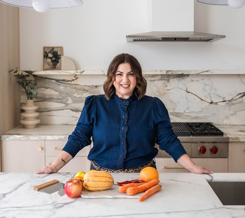 Mary Mammoliti se tient dans un studio de cuisine, devant des ingrédients frais disposés sur un comptoir en marbre.