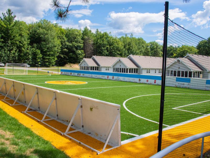 Le terrain de soccer du camp Lake Joe d'INCA est accessible. Il est équipé de plinthes tout autour du périmètre, de bordures texturées en coques de noix et d'un filet derrière les buts.
