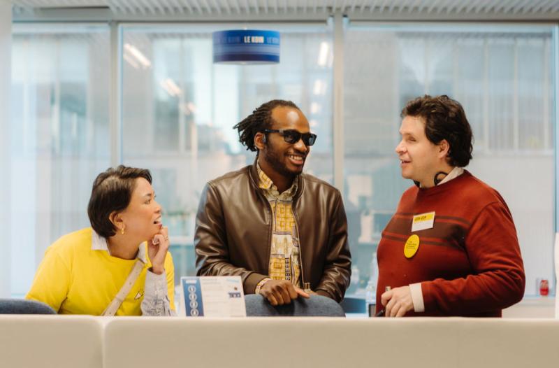 Trois membres du personnel et bénévoles d'INCA sourient et discutent derrière une table sur laquelle sont disposés divers dépliants.