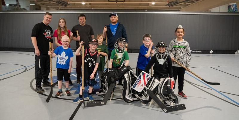 Un groupe d'enfants et le personnel de Hockey sonore Canada posent pour une photo dans un gymnase. Les participants ont le teint clair à moyen, et les enfants portent des équipements de hockey en salle.