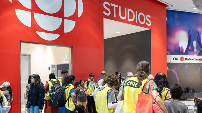 Au Maison de Radio-Canada à Toronto, un groupe important de jeunes campeurs et de bénévoles d'INCA se rassemble dans un studio. Derrière eux, on peut voir le logo de la Radio-Canada et le mot « studios »  peints sur le mur.  