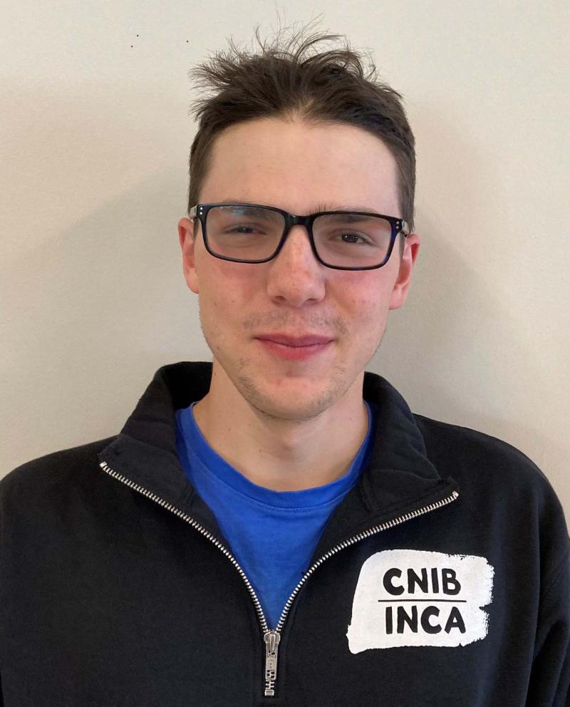 Curtis Ruttle portant un chandail CNIB/INCA. Curtis porte des lunettes, a le teint clair et les cheveux bruns.