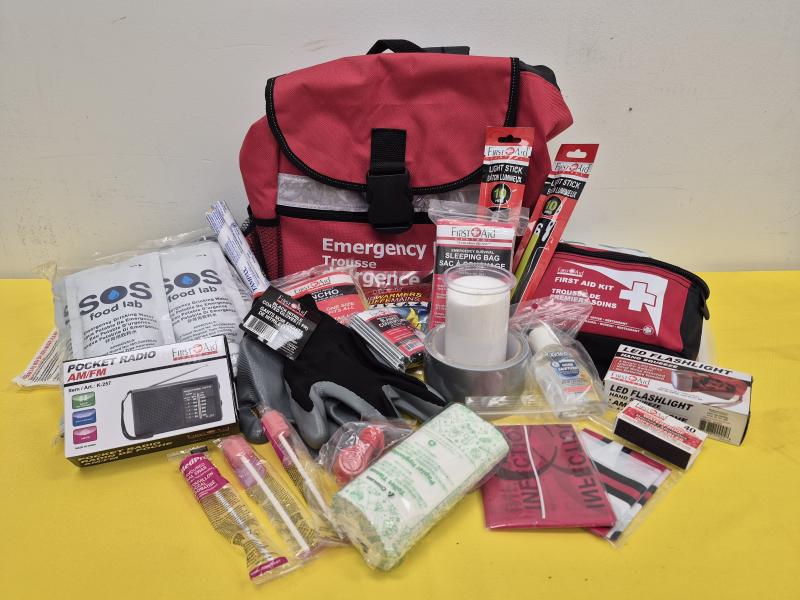 Le contenu d'une trousse d'urgence est étalé sur une table. Elle comprend une lampe de poche à DEL, une couverture de survie, une radio de poche, du désinfectant pour les mains, des sachets de nourriture SOS, etc.