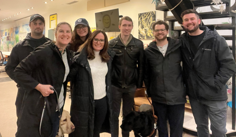 Une photo de groupe de Larissa et Shannon en compagnie de quatre membres de l'équipe de production de la vidéo de la Police de l'Ontario et de Jack, un utilisateur d'un chien-guide qui apparaît dans la vidéo, au GTA Community Hub. Larissa et Jack sont accompagnés de leurs chiens-guides.