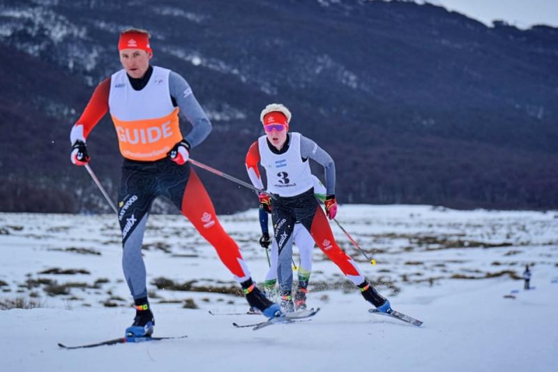Logan et son guide skient ensemble au sommet d'une montagne enneigée.