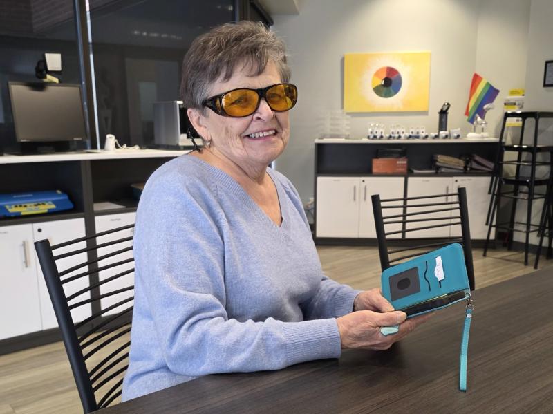 Une femme d'un certain âge portant des lunettes aux verres ambrés et tenant un téléphone intelligent adapté dans un étui bleu sarcelle.