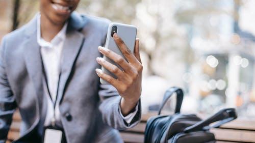 Femme noire assise sur un banc de parc, portant une veste d'affaires et tenant son téléphone intelligent.