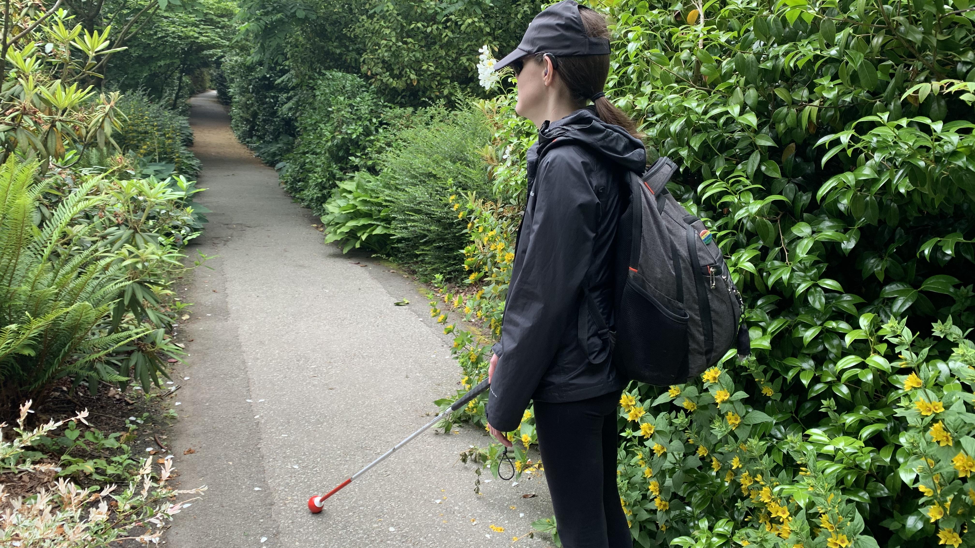 Abby marche le long d'un sentier verdoyant et s'oriente à l'aide de sa canne blanche. Abby se détourne de la caméra