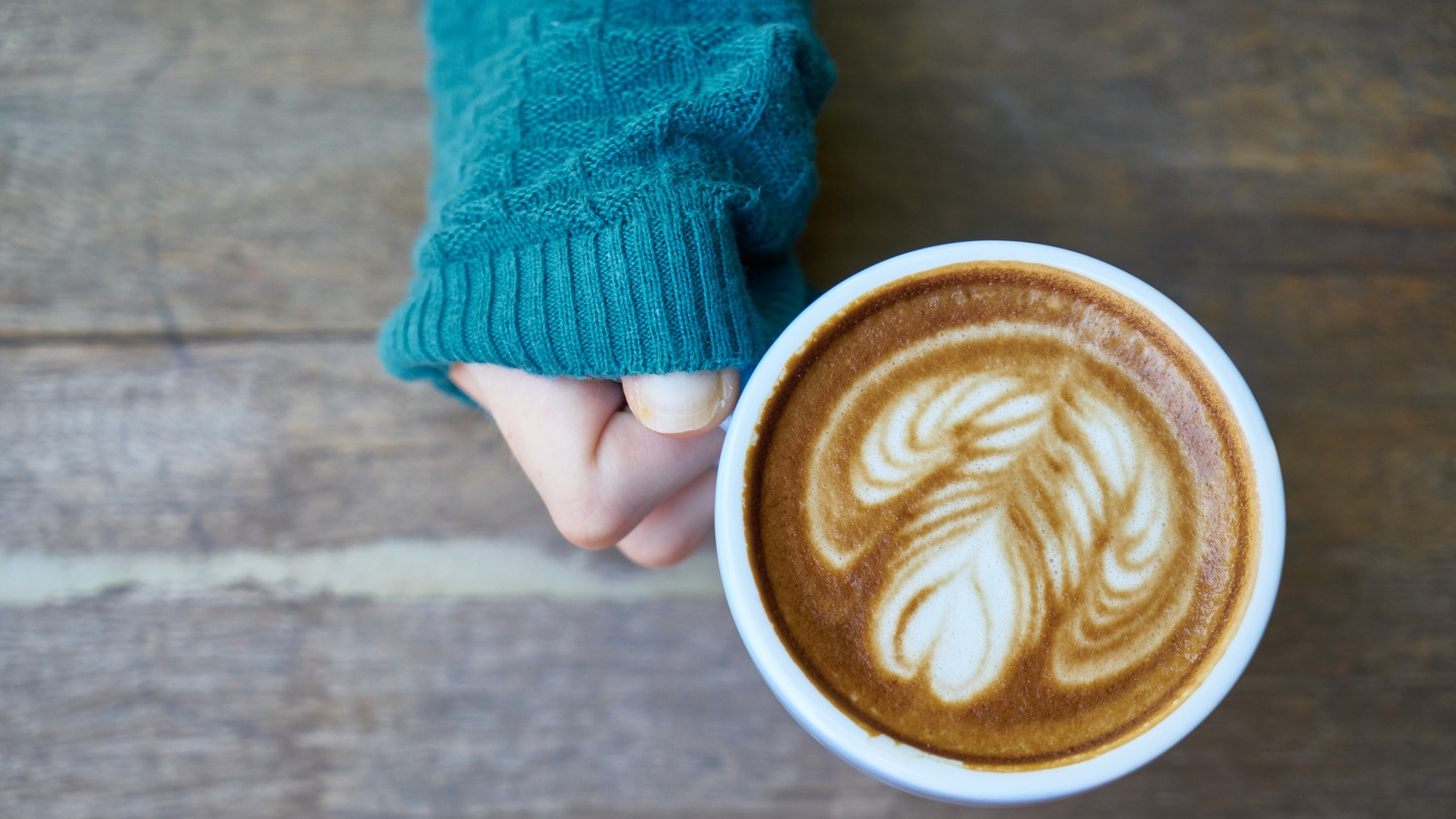 Une main tenant un café latté avec un dessin de coeur dans le lait.