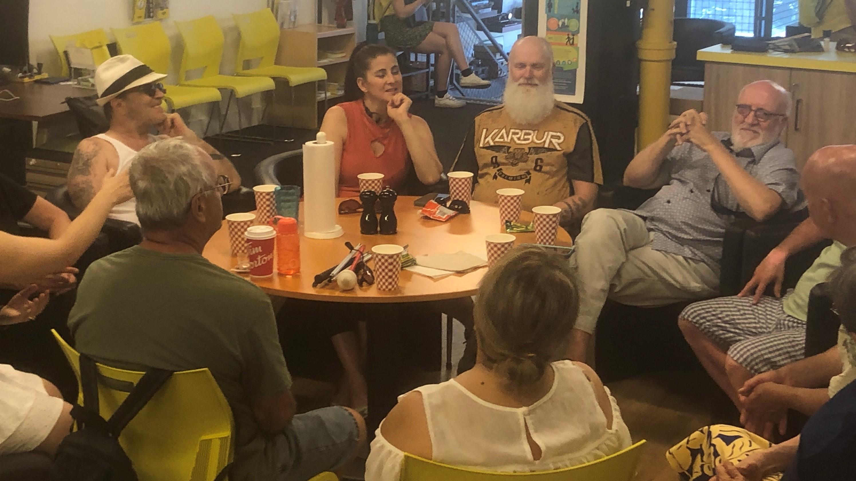 Groupe d'une dizaine de personnes confortablement assis autour d'une table à INCA discutant en souriant.