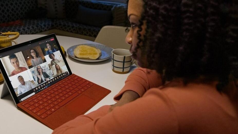 Une femme assise à une table avec un café participe à une rencontre de groupe sur son ordinateur. Les autres participants sont en vidéos.