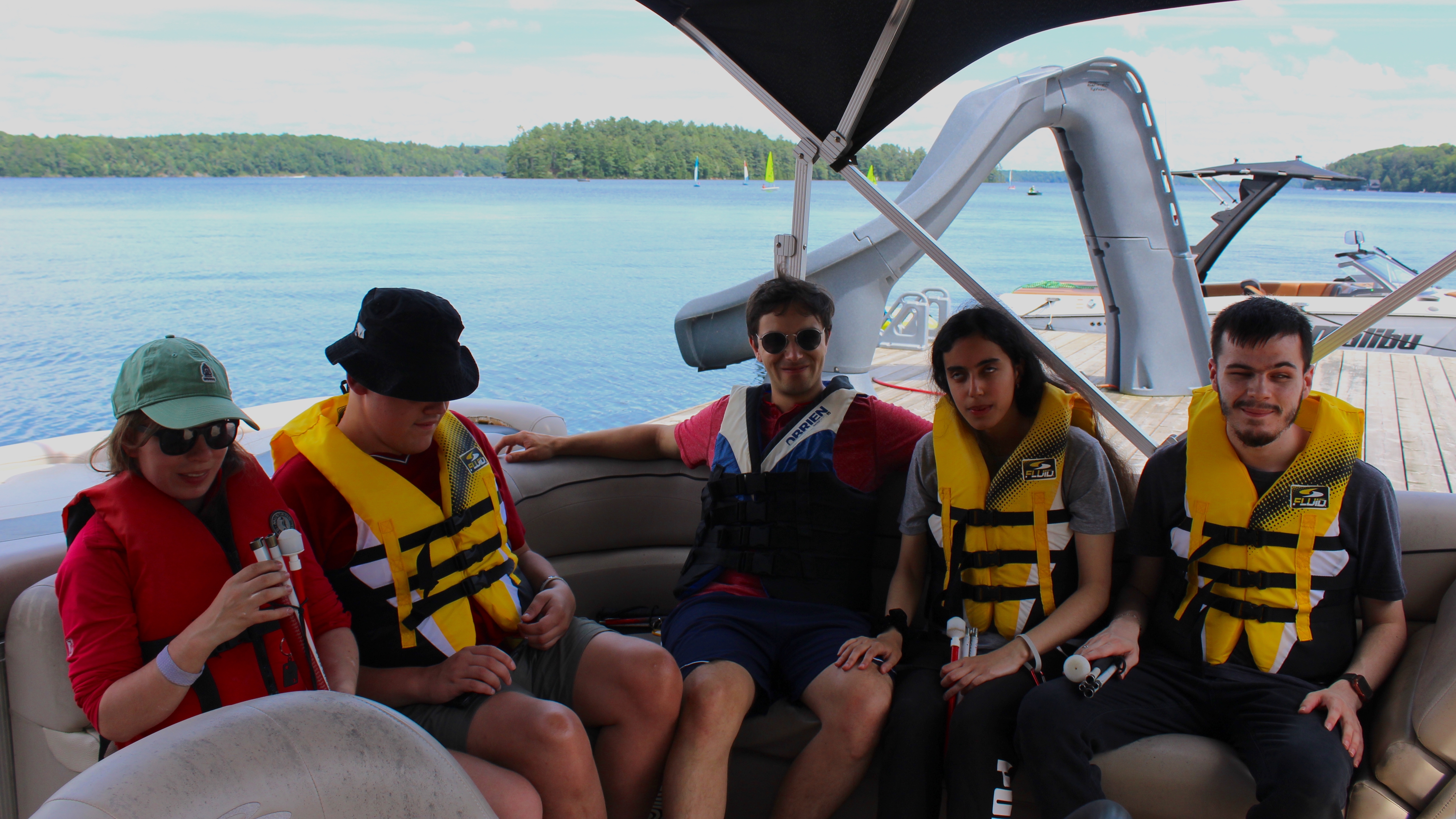 5 jeunes adultes portant une veste de sauvetage sur un bateau.