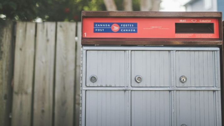 Boîte aux lettres de Postes Canada avec une clôture en bois derrière elle