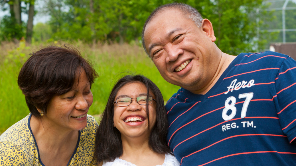 Une mère, un père et leur fille adolescente rient ensemble ; la fille porte des lunettes.