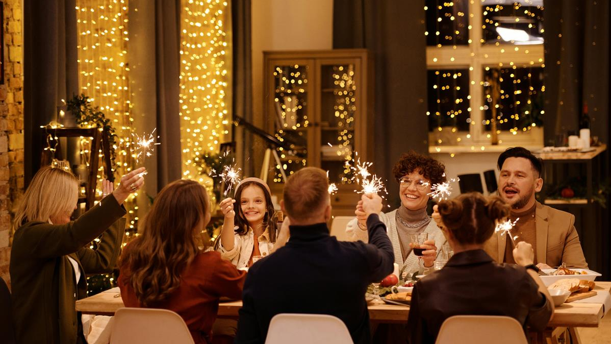 Une famille est à table et fête Noël. Pleins de guirlandes lumineuses sont accrochées aux fenêtres.