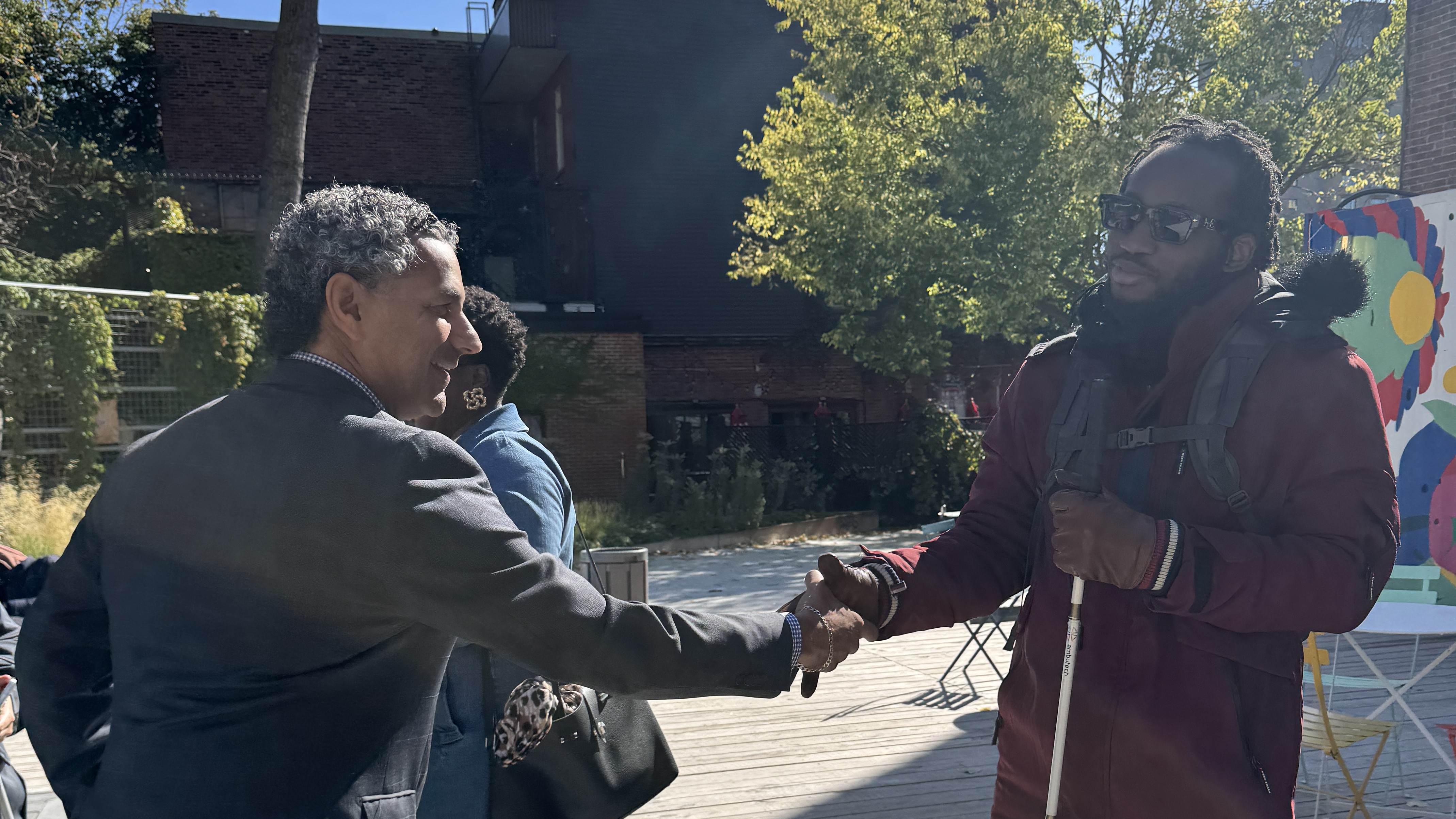 un candidat au municipal qui salue un homme en lunette noire et qui tient une canne blanche sur son autre main