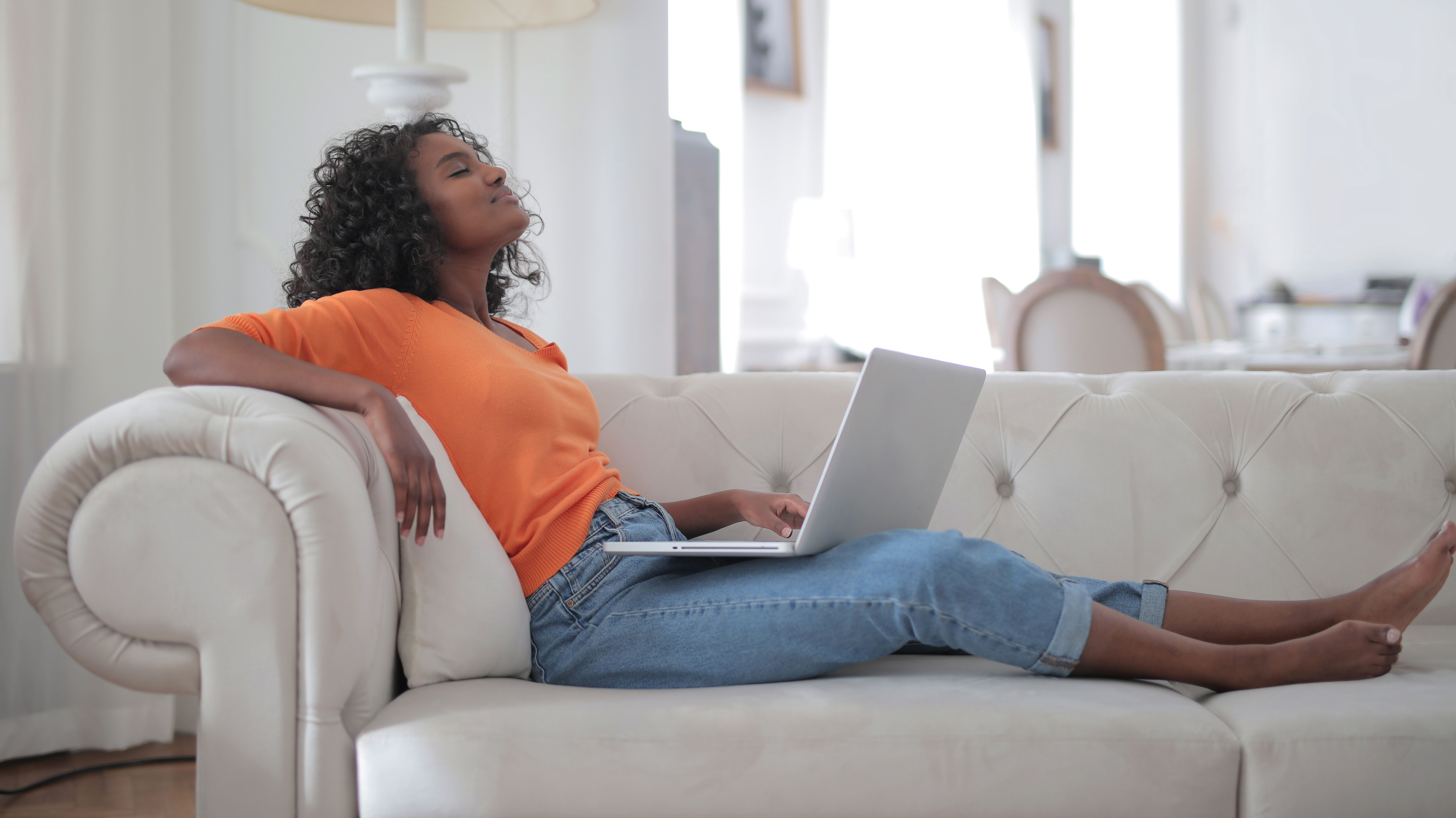 Une femme se détend sur son divan devant son ordinateur.