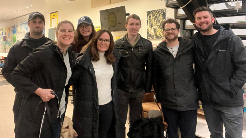 Une photo de groupe de Larissa et Shannon en compagnie de quatre membres de l'équipe de production de la vidéo de la Police de l'Ontario et de Jack, un utilisateur d'un chien-guide qui apparaît dans la vidéo, au GTA Community Hub. Larissa et Jack sont accompagnés de leurs chiens-guides.